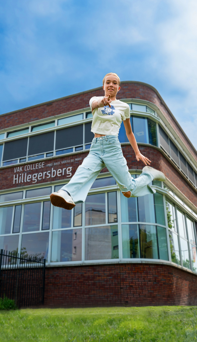 Leerling springt in de lucht voor de school, terwijl ze wijst naar de camera